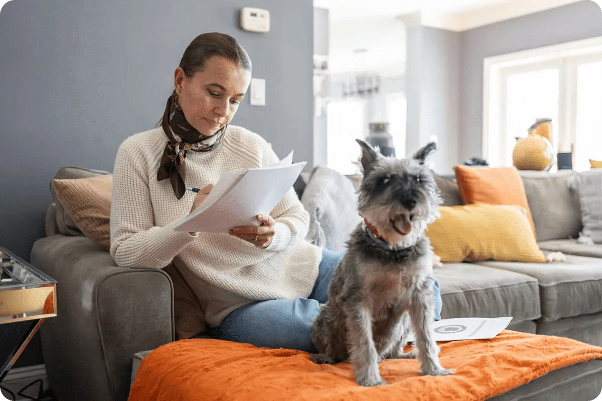 Woman reading papers with her attentive dog nearby on the couch.