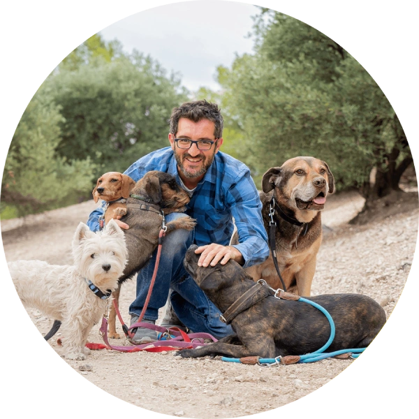 Man happily posing with four dogs outdoors on a dirt path.